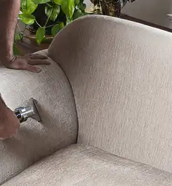 Professional upholstery cleaner deep-cleaning a fabric sofa with a handheld extraction tool and hose Evansville, IN.