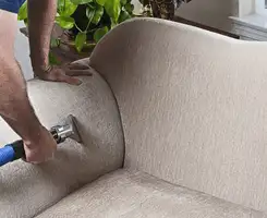 Professional upholstery cleaner deep-cleaning a fabric sofa with a handheld extraction tool and hose in Evansville, IN.